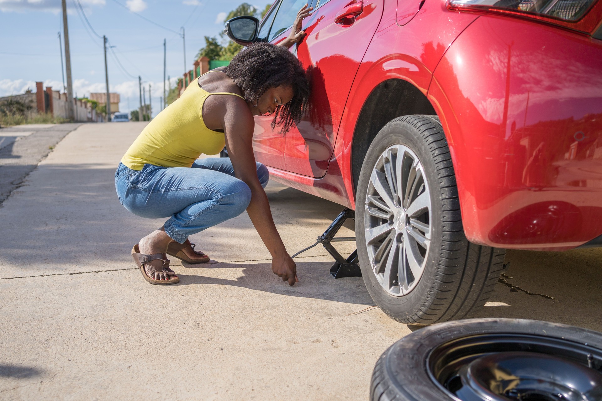 Woman stranded on the side of the road changing a flat tire